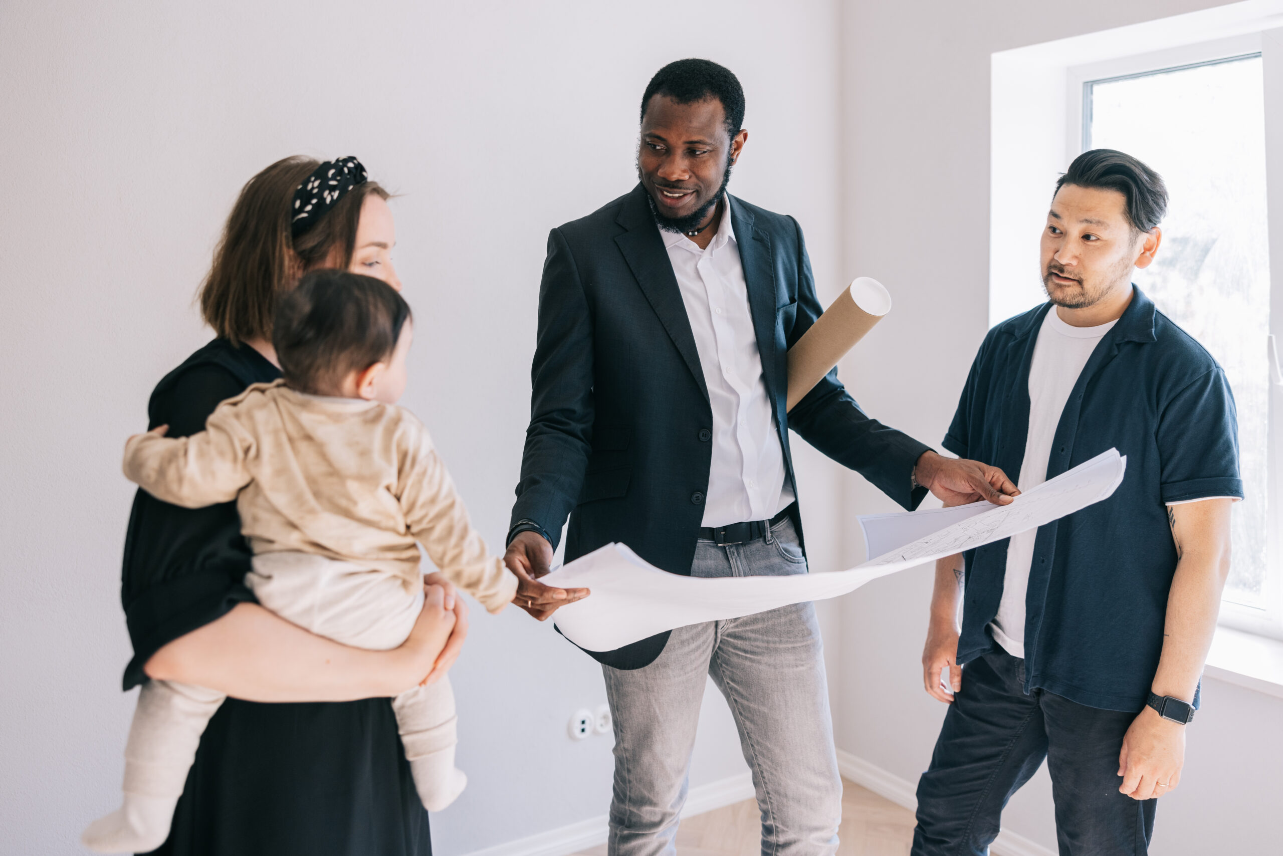 Multi-racial young family and Real Estate AGent, looking together at potential home blueprints.